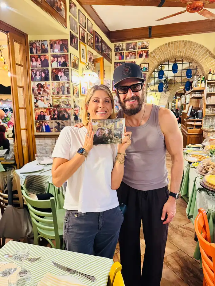 A bearded man in a cap and a smiling woman hold up a printed photo inside the restaurant
