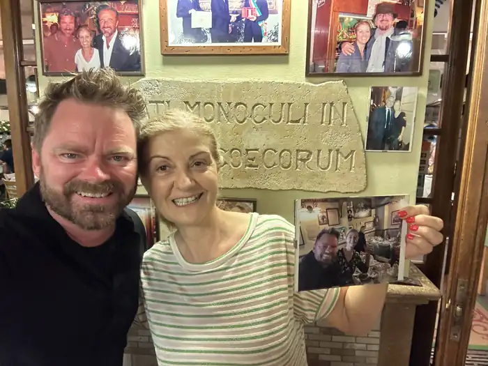 A selfie in front of the restaurant's photo wall, with a woman holding up a printed photo
